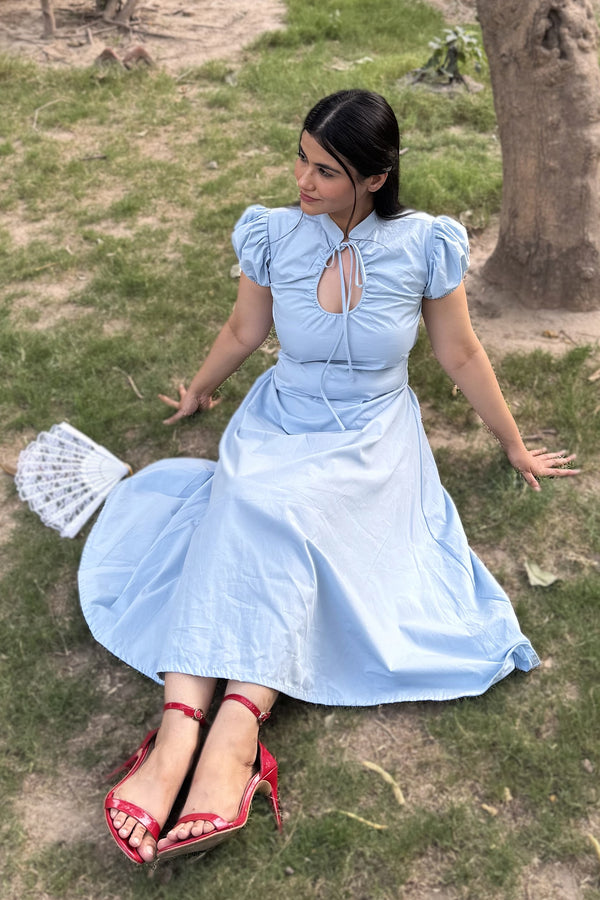 rooshy Blue Elan Collar Dress - model seated on grass holding white fan in sky blue collar midi dress